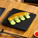 A matte black square stoneware flat plate with food arranged on top.