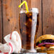 A glass of Narvon Diet Cola with ice and a straw next to a burger on a wooden table.