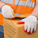 A person wearing Cordova natural and red latex work gloves opening a box.