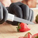 A person in black gloves using a Choice Hotel Style Paring Knife to cut a strawberry.
