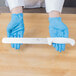 A person in blue gloves using a Choice white straight edge slicing knife to slice meat on a wooden cutting board.