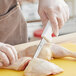 A person in gloves using a Choice narrow stiff boning knife with white handles to cut up a chicken.
