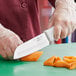 A gloved hand uses a Choice Santoku knife to slice carrots.