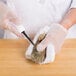 A gloved hand uses a Choice New Haven Style Oyster Knife with a white handle to cut an oyster.