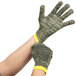 A pair of Cordova Camo Cut Resistant gloves with yellow and black stripes on the cuffs being worn by a pair of hands.