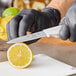 A person in black gloves using a Choice 4" Smooth Edge Paring Knife with a white handle to cut a lemon.