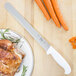A Choice white straight edge slicing knife next to a plate of meat and carrots.
