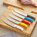 A group of Choice cimeter knives with white handles on a cutting board with meat and vegetables.