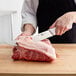 A person using a Choice 10" Cimeter Knife to cut meat on a wooden surface.