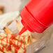 A close up of a red Choice wide mouth squeeze bottle of ketchup over french fries.