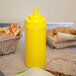 A yellow Choice wide mouth squeeze bottle next to a sandwich on a table.