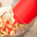 A red Choice squeeze bottle pouring ketchup over french fries.