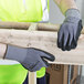 A person wearing Cordova Conquest Plus gloves with black foam nitrile and nitrile dots holding a piece of wood.