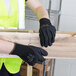 A person wearing Cordova black foam nitrile/polyurethane gloves and a yellow vest holding a piece of wood.