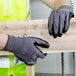 A person wearing Cordova gray gloves with black palm coating holding a piece of wood.