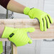 A person wearing Cordova lime green gloves with canvas palm coating holding a piece of wood.