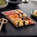 An Acopa rectangular stainless steel tray with sushi rolls and chopsticks on a table.