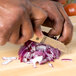 A person using a Town onion knife to cut a red onion on a cutting board.