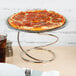 An Acopa stainless steel swirl metal display stand holding a pepperoni pizza on a white table.