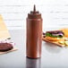 A brown Choice wide mouth squeeze bottle on a table next to a sandwich.