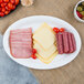 A white plastic oval catering tray with sliced meat, cheese, and tomatoes.
