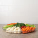 A Fineline clear plastic 7-compartment tray with vegetables including carrots, broccoli, and celery.