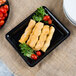 A Fineline black plastic rectangular catering tray with food on it.