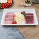 A Fineline white rectangular plastic catering tray with meat, cheese, and vegetables on it.