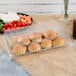 A Fineline clear plastic rectangular catering tray with brown food and cherry tomatoes on a table.