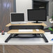 A Luxor white oak stand up desktop desk with a laptop and monitor on the top tier.