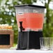 A black Choice beverage dispenser with glasses filled with juice.