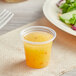 A plastic cup of orange liquid next to a plate of salad.