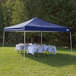 A Caravan Canopy tent set up with tables and chairs on grass with a white tablecloth on one table.
