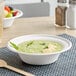 A white EcoChoice compostable bagasse bowl filled with green soup on a place mat.