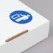 A white square corrugated cardboard lid with a blue circle and a pictogram on it.