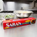 A red box of SC Johnson Saran Premium Plastic Wrap on a kitchen counter with a bowl of salad wrapped in plastic.
