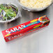 A bowl of salad wrapped in SC Johnson Saran Premium plastic wrap next to a box of food.