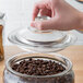 A hand opening a Choice 0.75 Gallon Glass Jar filled with coffee beans.