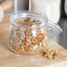 A Choice glass storage jar filled with granola on a cutting board.