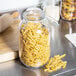A Choice 105 oz. glass storage jar with pasta on a kitchen counter.