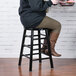 A woman sitting on a Lancaster Table & Seating black metal counter height stool at a counter.