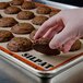 A hand holding a chocolate cookie over a Sasa Demarle SILPAT baking mat on a tray of cookies.