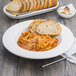 A Fiesta white china pasta bowl filled with pasta with sauce and a piece of bread on the side.