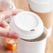 A hand holding a white plastic lid of a coffee cup.