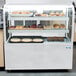 A bakery display case with pastries and an Avantco LED lamp inside.