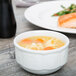 A Tuxton bright white china bouillon cup filled with soup next to a plate of food.