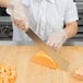 A person in white gloves using a Dexter-Russell Sani-Safe white handled cheese knife to cut a slice of cheese.