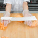 A person in a plastic glove using a Dexter-Russell white handled cheese knife to cut cheese.