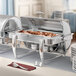 A buffet table with Acopa stainless steel chafers full of food and silverware.