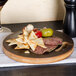 An American Metalcraft carbonized bamboo round serving board with meat, cheese, and crackers on a table.